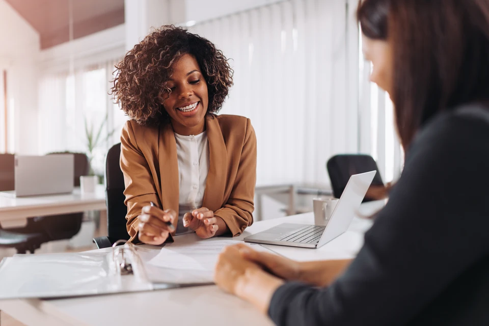 Contrat avec les meilleures conditions ! Jeune homme confiant en chemise et cravate tenant un document et le pointant avec le sourire tout en étant assis avec le jeune couple au bureau